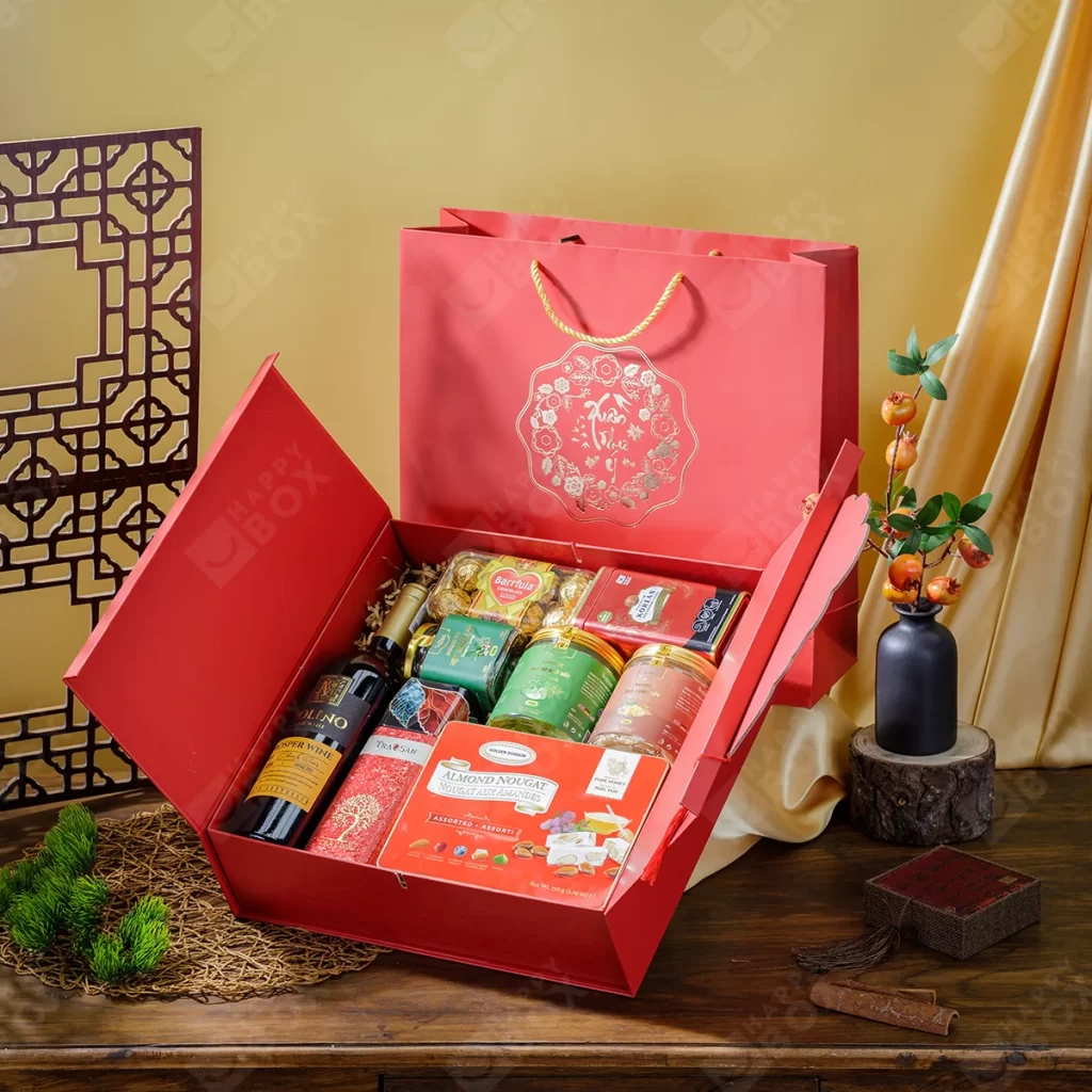 Hộp quà tết màu đỏ nắp gập mở ra với rượu vang, trà, bánh kẹo, kèm túi giấy